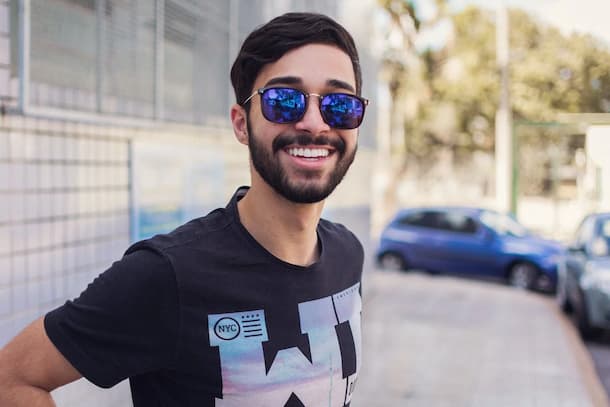 hombre joven sonriendo a la camara en la calle, con lentes de sol