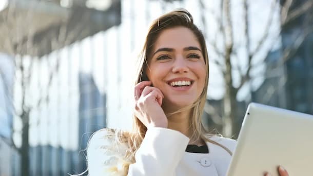 Mujer joven soriendo, hablando por telefono y sosteniendo una tablet en una de sus manos