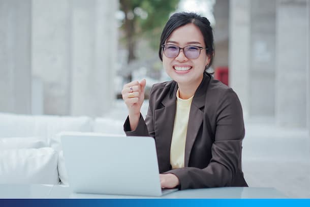 mujer sonriendo, sentada con su notebook abierto sobre la mesa y con lentes puestos