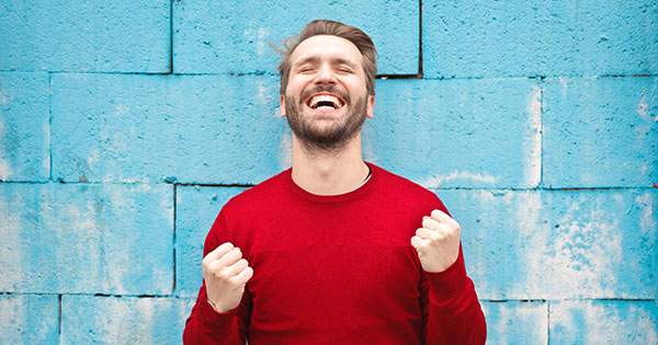 hombre extremadamente feliz, sonrie con los ojos cerrados y con ambas manos empuñadas