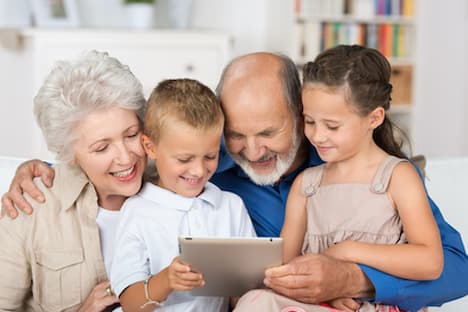 abuelos con sus dos nietos felices y abrazados mirando una tablet